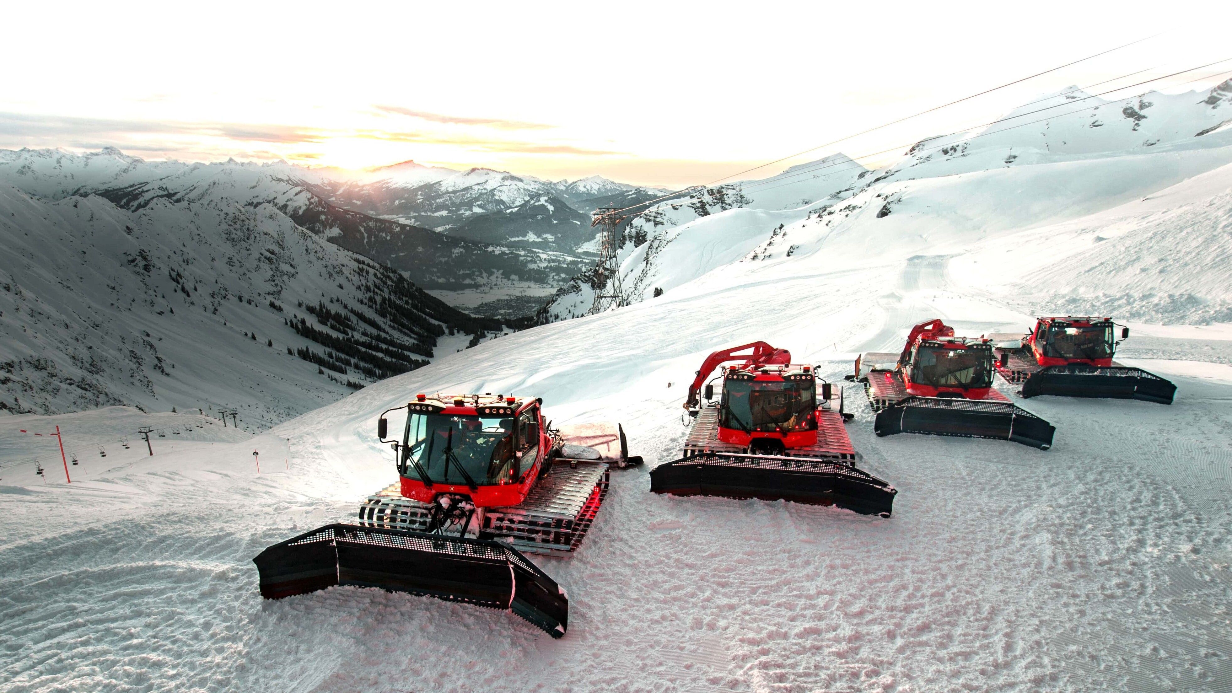 Vier PistenBully 600 vor einer wunderschönen Bergkette.