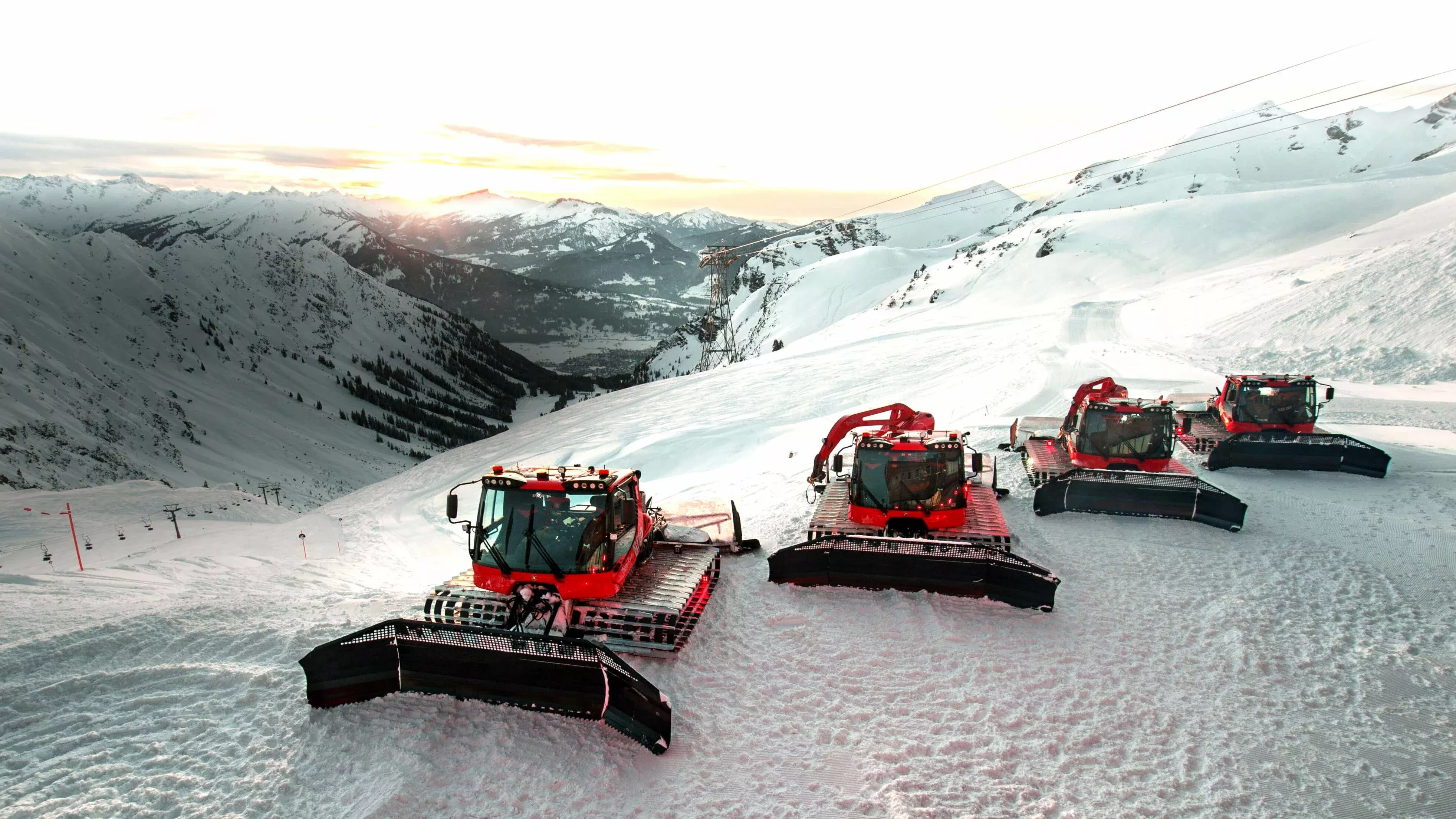 Quatre PistenBully 600 devant une belle chaîne de montagnes.